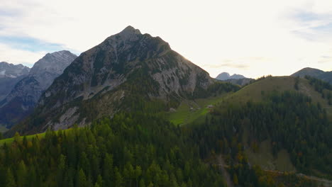 Aerial-view-orbiting-Karwendel-Tyrol-forested-mountains-as-sun-appears-from-behind-idyllic-peaks
