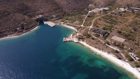 Luftvorbeiflug-über-Einen-Türkisfarbenen-Strand-Mit-Verlassenen-Kommunistischen-Strukturen-An-Der-Albanischen-Riviera