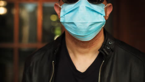 Man-standing-outside,-wearing-a-covid-19-surgical-mask-and-sunglasses