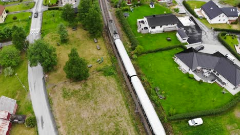 Aerial:-Flåm-train-going-through-a-valley-among-green-meadows-and-some-houses