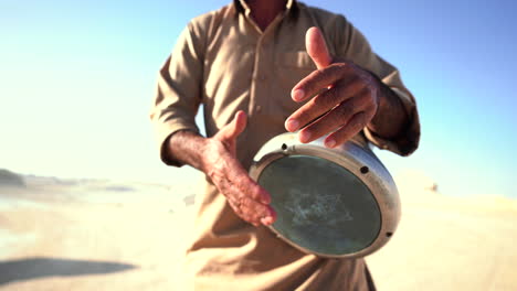 close-up-of-skilled-musician-performing-local-music-playing-hand-drum-with-sand-dunes-in-background