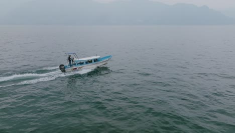 Tracked-aerial-footage-following-and-passing-a-passenger-speedboat-that-is-going-across-the-water-of-Lake-Atitlan-in-Guatemala-in-the-haze