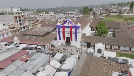Aerial-footage-that-is-moving-towards-the-Iglesia-de-Santo-Tomás-in-Chichicastenango,-Guatemala-with-Easter-colors-covering-the-facade