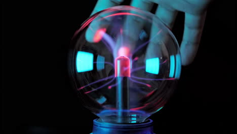 Close-up-hand-attracting-a-plasma-filament-on-a-plasma-ball,-Hand-touching-with-finger-electric-plasma-ball-with-luminous-flames-in-dark-room