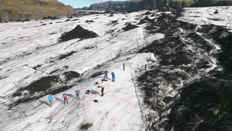 Low-reverse-aerial-dolly-flying-over-hikers-exploring-Icelandic-glacier