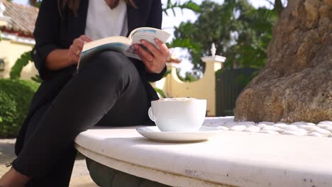 Young-professional-woman-reading-a-book-outside-in-nature-with-a-coffee-cup