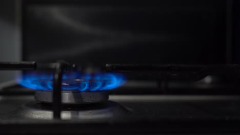 Gasherd-Brennt-Blaue-Flamme,-Während-Die-Defokussierte-Hand-Im-Hintergrund-Den-Knopf-Dreht