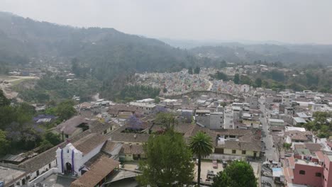Luftaufnahmen-Von-Links-Nach-Rechts-In-Der-Stadt-Chichicastenango-Mit-Einer-Kirche-Im-Vordergrund-Und-Dem-Farbenfrohen-Friedhof-Im-Hintergrund