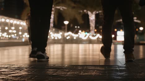 Hombres-Caminando-En-La-Calle-Nocturna,-Luces-Y-Palmeras