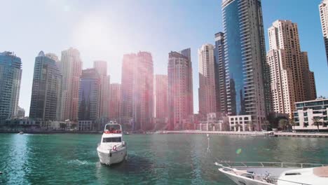 Boat-Arrives-Dockside-Under-Modern-Towers,-Skyscrapers-in-Dubai