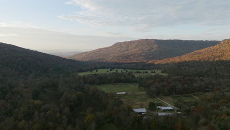 Aerial-footage-of-a-farm-that-is-in-shadow-with-mountains-being-covered-by-a-rising-sun-in-Sequatchie-Cove-Tennessee-in-Autumn