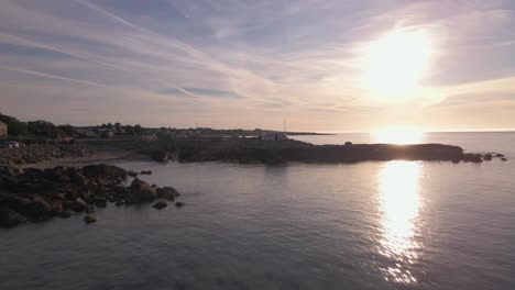 Luftaufnahmen-Von-Drohnen-An-Der-Küste-In-Irland,-Während-Sie-Bei-Sonnenuntergang-Die-Küstenfelsen-überqueren,-Vögel,-Die-Im-Wasser-Mit-Strahlendem-Himmel-Herumfliegen