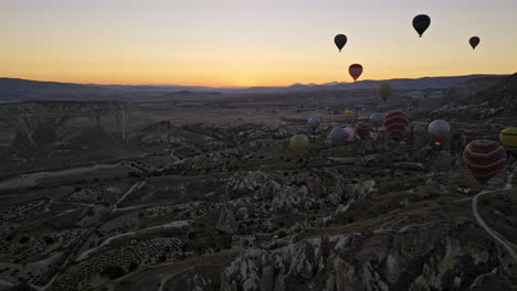 Göreme-Turkey-Aerial-v45-sunrise-landscape-capturing-surreal-volcanic-rock-formations-with-touristic-adventure-hot-air-balloons-ride-rising-into-the-sky-at-dawn---Shot-with-Mavic-3-Cine---July-2022