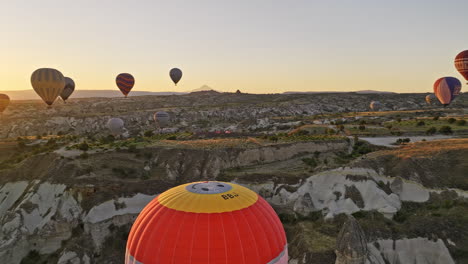 Göreme-Turkey-Aerial-v55-panoramic-view-capturing-cave-town,-chimney-rock-formations-with-hot-air-balloons-in-the-sky-and-sun-rising-behind-mesa-tableland-mountain---Shot-with-Mavic-3-Cine---July-2022