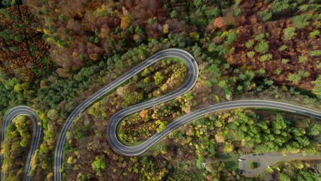 Aerial-drone-video-pointing-down-a-winding-mountain-road-with-cars-and-motorbikes-driving-carefully,-surrounded-by-a-forest-with-autumn-in-the-mountains-of-Bieszczady-in-Poland,-Europe