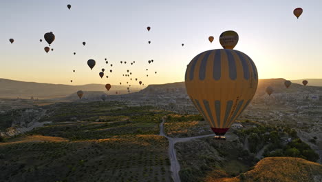 Göreme-Turkey-Aerial-v58-panoramic-panning-view-of-unique-plateau-fields-with-sun-rising-up-behind-mesa-mountain-with-colorful-hot-air-balloons-flying-in-the-sky---Shot-with-Mavic-3-Cine---July-2022