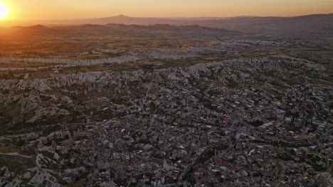 Göreme-Turkey-Aerial-v4-birds-eye-view,-flyover-ancient-village-town-capturing-vastness-of-cappadocia-surreal-landscape-with-glowing-sun-setting-in-the-horizon---Shot-with-Mavic-3-Cine---July-2022