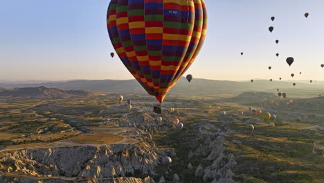 Göreme-Turkey-Aerial-v63-close-up-fly-around-colorful-hot-air-balloon-with-tourists-taking-scenic-sunrise-flight-with-panoramic-view-of-rock-formations-landscape---Shot-with-Mavic-3-Cine---July-2022