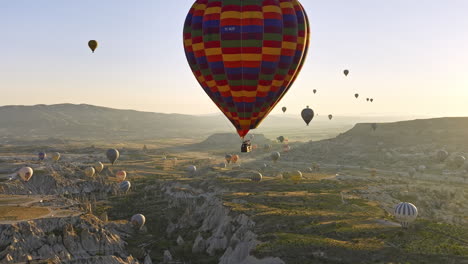 Göreme-Turkey-Aerial-V64-Bemerkenswerte-Landschaft-Des-Weltnaturerbes-Mit-Einzigartiger-Felsformation,-Tal,-Hochebenenfeldern-Und-Heißluftballons-Am-Himmel-Bei-Sonnenaufgang---Aufgenommen-Mit-Mavic-3-Cine---Juli-2022