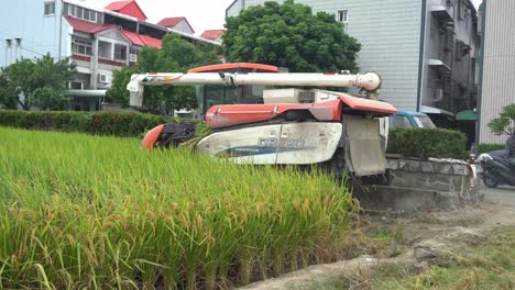 Multifunctional-machine-rice-harvester-tractor-driving-across-cultivated-rice-paddy-field,-harvesting-crops-reaping,-threshing,-and-winnowing-at-Douliu-city,-Yunlin-County,-Taiwan