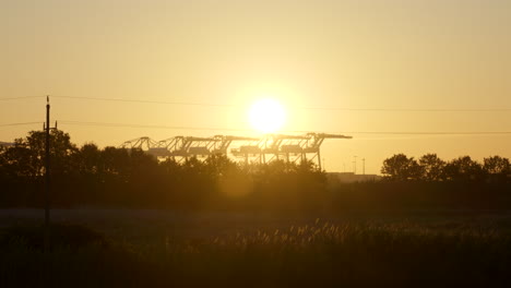 Sonnenaufgang,-Der-über-Hafenkränen-Der-Industriewerft-Und-Bäumen-Am-Horizont-Scheint