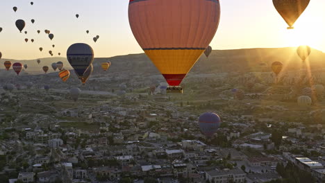Göreme-Turkey-Aerial-v61-flyover-old-town-capturing-colorful-hot-air-balloons-ride-in-the-sky,-zoom-out-reveals-beautiful-sunrise-landscape-with-golden-glowing-sun---Shot-with-Mavic-3-Cine---July-2022