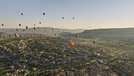 Göreme-Turkey-Aerial-v70-magical-golden-sunrise-view,-flyover-rock-site-capturing-formation-of-plateau-fields-and-fairy-chimneys,-with-hot-air-balloons-in-the-sky---Shot-with-Mavic-3-Cine---July-2022