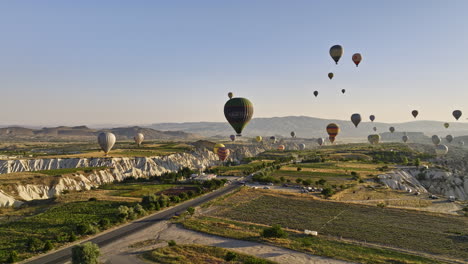 Göreme-Turkey-Aerial-v73-wonders-of-the-world,-low-flyover-plateau-fields-capturing-chimney-rocks-and-valleys-with-dreamy-hot-air-balloons-in-the-sky-at-sunrise---Shot-with-Mavic-3-Cine---July-2022