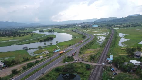 Aerial-drone-shot-flying-over-highway-parallel-to-railway-track-carved-through-farming-land,-Asia