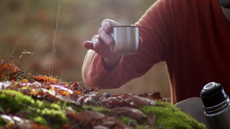 Tourist-man-drinking-hot-tea-or-coffee-in-forest,-close-up-view-of-hand-holding-thermos-mug