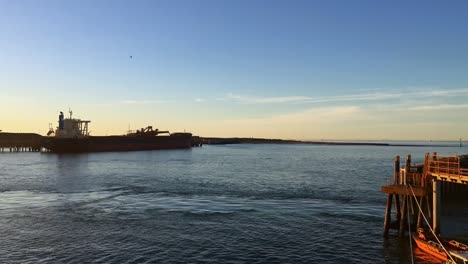 Timelapse-of-tugboats-moving-near-a-dock-during-a-sunset-in-a-clear-day