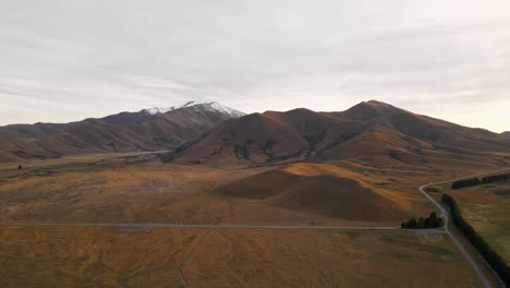 Empty-curved-highway-on-a-high-altitude-mountain-plateau-in-New-Zealand-during-golden-hour