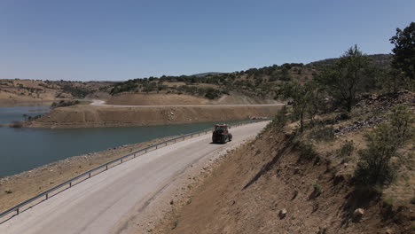 Drone-Siguiendo-A-Un-Camionero-Rojo-Conduciendo-Lentamente-Por-Una-Carretera-En-Turquía-Karaman-Entre-El-Lago-Azul-Y-Las-Montañas-En-Un-Verano-Soleado-Aunque-Con-Curvas