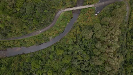 Top-down-aerial-view-following-the-course-of-a-jungle-river-with-a-small-bridge-crossing