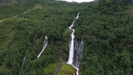 Stunningly-beautiful-Yrielva-river-coming-from-the-Myklebust-glacier-is-forming-a-waterfall-in-lush-dark-green-forest-on-its-way-down-the-mountainside---Norway