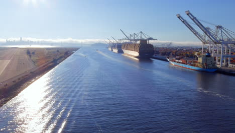 Flying-along-the-canal-to-the-Port-of-Oakland-in-California-with-cargo-ship-being-loaded-or-unloaded-with-shipping-containers-by-cranes