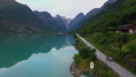 Tourist-drive-along-Olden-lake-road-with-the-Briksdal-glacier-in-background-mountain-top---Aerial-following-car-on-vacation-journey-along-stunningly-beautiful-landscape