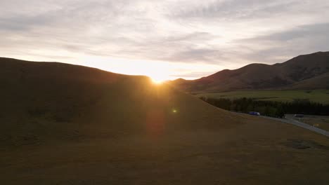 Cinematic-flight-towards-the-golden-sun-peeking-out-behind-a-mountain-range-in-rural-New-Zealand