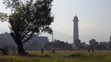 A-group-of-young-people-playing-cricket-in-the-shadow-of-the-Dharahara-Tower-in-Kathmandu,-Nepal