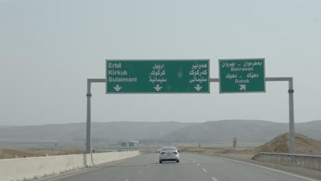 Driving-past-a-highway-sign-in-Kurdistan-Iraq-for-Erbil,-Kirkuk,-Sulaimani,-and-Duhok