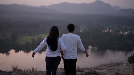 A-beautiful-couple-in-white-dress-taking-long-breathe-near-a-lake-and-mountain-range-at-sunset