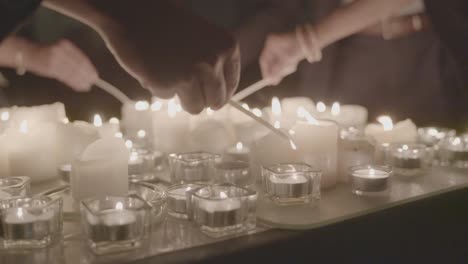 Mehrere-Personen-Zünden-Bei-Einer-Kirchlichen-Zeremonie-Einen-Tisch-Voller-Kerzen-An