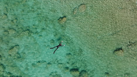 Twisting-top-down-aerial-of-snorkeler-on-back-in-crystal-clear-ocean
