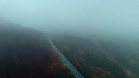 Long-winding-road-with-passing-cars-through-natural-scenery-on-a-cold-autumn-morning