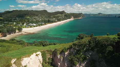 Aerial-view-of-clouds-rolling-over-Te-Pare-bluff-in-Hahei,-New-Zealand