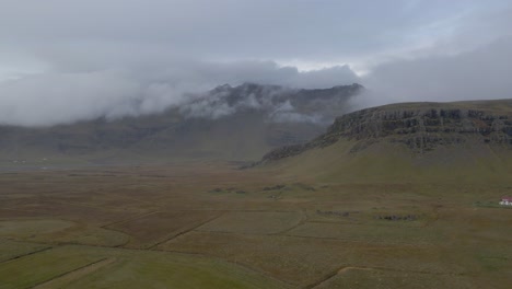 Verdant-and-flat-Icelandic-landscape-with-mountains-shrouded-low-clouds,-Iceland