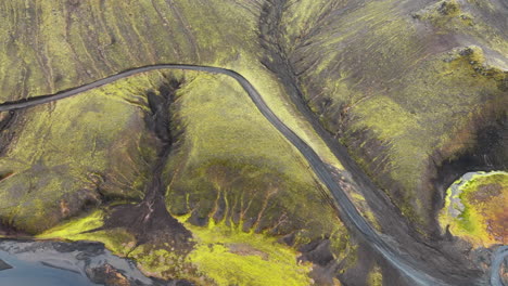 Aerial-view-of-highway-running-through-mossy-hills,-mountains-in-Iceland