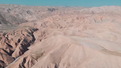 Drone-cinematic-tilt-down-shot-of-a-desert-green-mounts,-Jurassic-park-look,-blue-sky