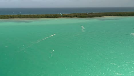 Aerial-pan-left-people-kiteboarding-on-caribbean-sea,-near-tropical-mangrove-Los-Roques