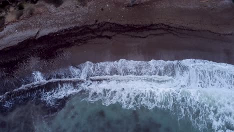 Top-down-aerial-moving-forward-of-waves-on-dark-beach,-Cala-Tuent,-Mallorca